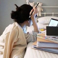 a woman sitting on a bed holding a pen in her hand and looking at a laptop