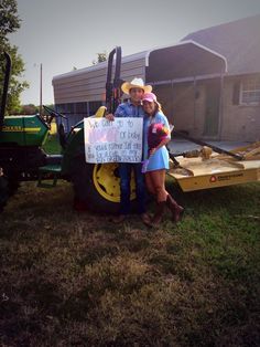 two people standing in front of a tractor holding a sign