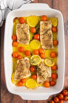 fish with lemons, tomatoes and cherry tomatoes in a white casserole dish