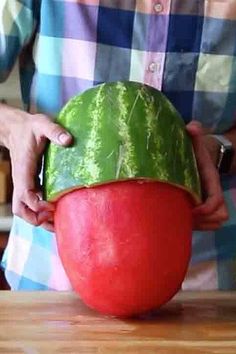 a man holding a large watermelon on top of a wooden table