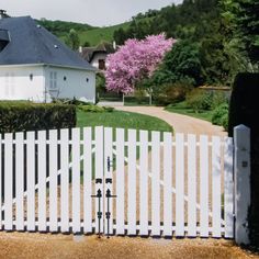 a white picket fence in front of a house with pink flowers on the trees behind it