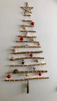 a christmas tree made out of wooden sticks and lights is hanging on the white wall