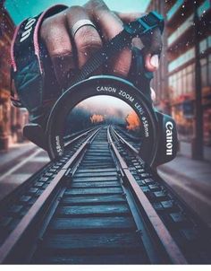 a hand holding a camera over train tracks