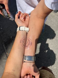 two people are holding hands with tattoos on their arms and wristbands, one has a compass tattoo on the other arm