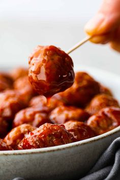 a person holding a spoon full of meatballs with sauce on them in a white bowl