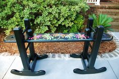 a bench that is sitting in front of some bushes and plants on the side walk