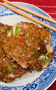 two fried meat patties on top of rice with chopsticks