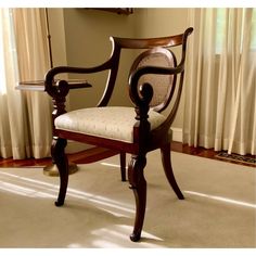 a wooden chair sitting on top of a carpeted floor next to a window with white curtains