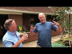 two men standing in front of a house talking to each other and holding their hands out