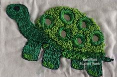 a close up of a green crocheted turtle on a white cloth with holes in the middle