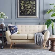 a living room filled with furniture and plants on the wall next to a painting hanging above it