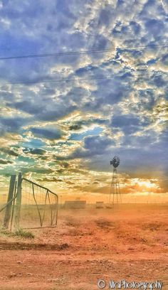 the sun is setting over an open field with windmills and water towers in the distance