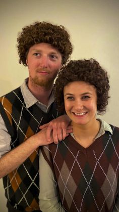 a man with curly hair standing next to a woman wearing a sweater vest and smiling at the camera