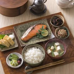 a wooden tray topped with different types of food next to cups and saucers on top of a table