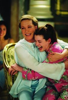 two women hugging each other while sitting on a chair in front of another woman and smiling