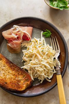 a plate with meat, cheese and bread on it next to a fork and knife