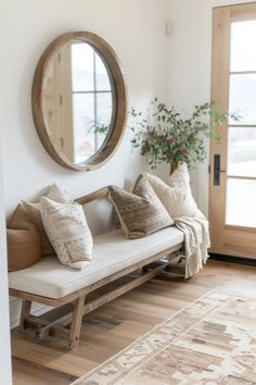 a wooden bench with pillows on it in front of a round mirror and potted plant