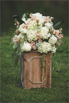 a wooden box filled with white and pink flowers on top of a grass covered field