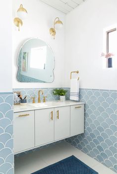 a bathroom with blue and white tiles on the walls, gold fixtures and a round mirror