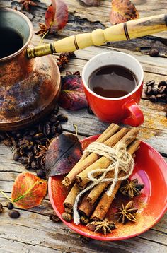 an orange plate topped with cinnamon sticks next to a cup of coffee and some leaves