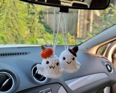 two crocheted ghost decorations hanging from the dashboard of a car