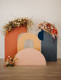 three different colored vases with flowers in them on a wooden floor next to each other