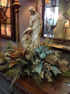 a christmas arrangement on top of a dresser next to a mirror with a statue in the background