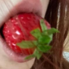 a close up of a woman's lips with a strawberry in her mouth and green leaf sticking out of the lip