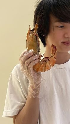 a young man holding up two pieces of food to his face while wearing gloves and white shirt