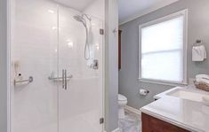 a bathroom with a walk in shower next to a white toilet and sink under a window