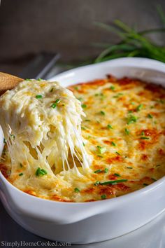 a wooden spoon scooping mashed potatoes from a casserole in a white dish