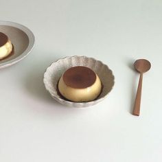 two small bowls with desserts in them on a white table top next to a wooden spoon