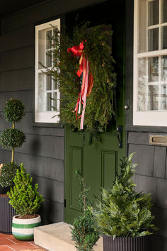 christmas wreaths are hanging on the front door of a house with potted trees