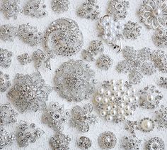 many different types of buttons and beads on a white cloth with silver sequins