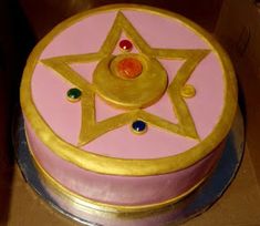 a pink and gold cake with a star decoration on the top is sitting in a box