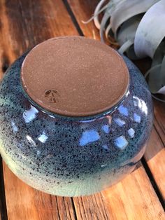 a blue and green vase sitting on top of a wooden table next to a plant