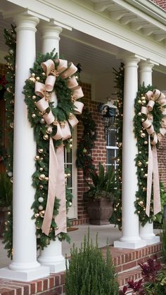 two wreaths on pillars decorated with lights and bows for the front door to welcome guests