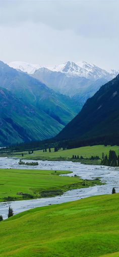 a river running through a lush green valley surrounded by snow covered mountain range in the distance