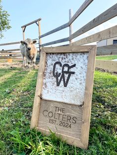 a cow standing next to a sign in the grass near a fence and wooden post