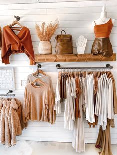 clothes and handbags are hanging on the rack in front of a white wooden wall