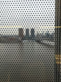 the view from inside an airport through a meshed window with buildings in the background