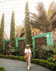 a woman is walking in front of some trees and plants at the gardens by the bay