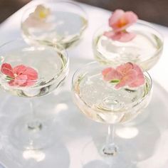 three wine glasses with flowers in them sitting on a white tablecloth and plated