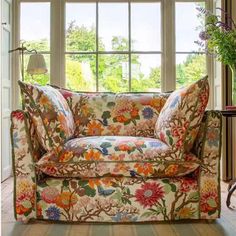 a floral couch sitting in front of a window next to a vase with flowers on it