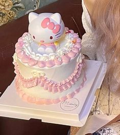 a hello kitty cake sitting on top of a white box next to a woman's face