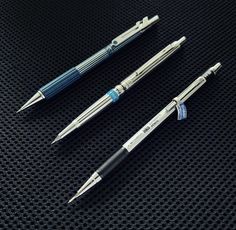 three pens sitting on top of a black surface