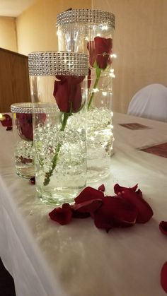 three vases filled with water and red roses on a white tablecloth covered table