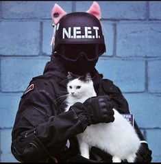 a person in a black jacket holding a white and black cat wearing a helmet on top of their head