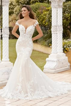 a woman in a white wedding dress standing on a brick walkway with columns and pillars behind her