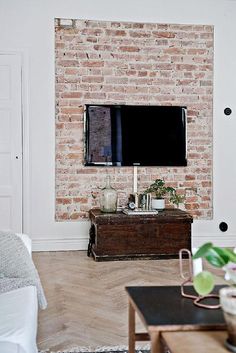 a flat screen tv mounted on a brick wall in a living room next to a coffee table